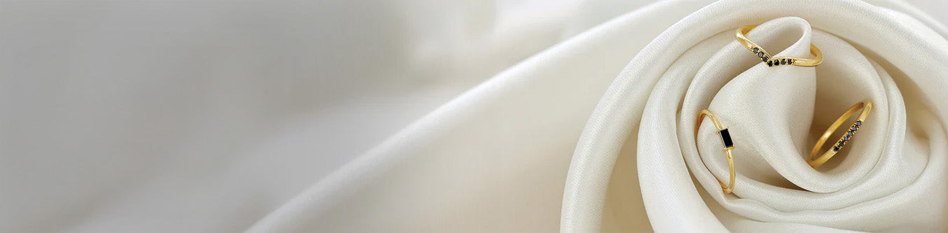 Fine yellow gold rings set with black diamonds on silky white fabric, modern jewellery collection