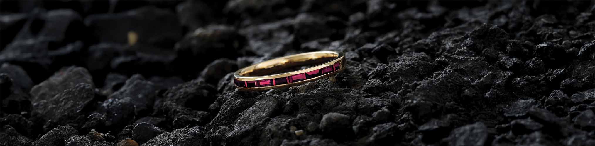 Yellow gold men's wedding ring set with rectangular baguette cut rubies on textured black volcanic stone