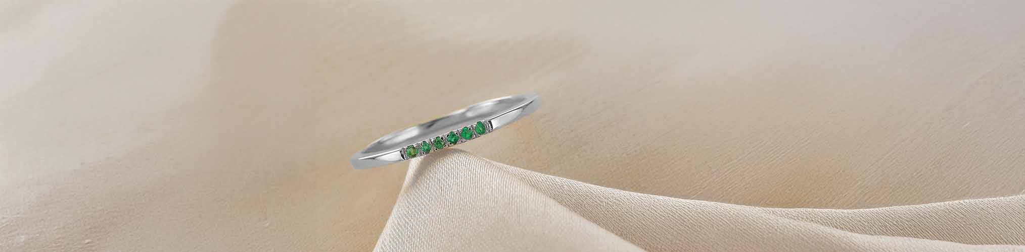 Silver wedding ring set with green emeralds in line, fine modern jewellery ring on delicate beige fabric