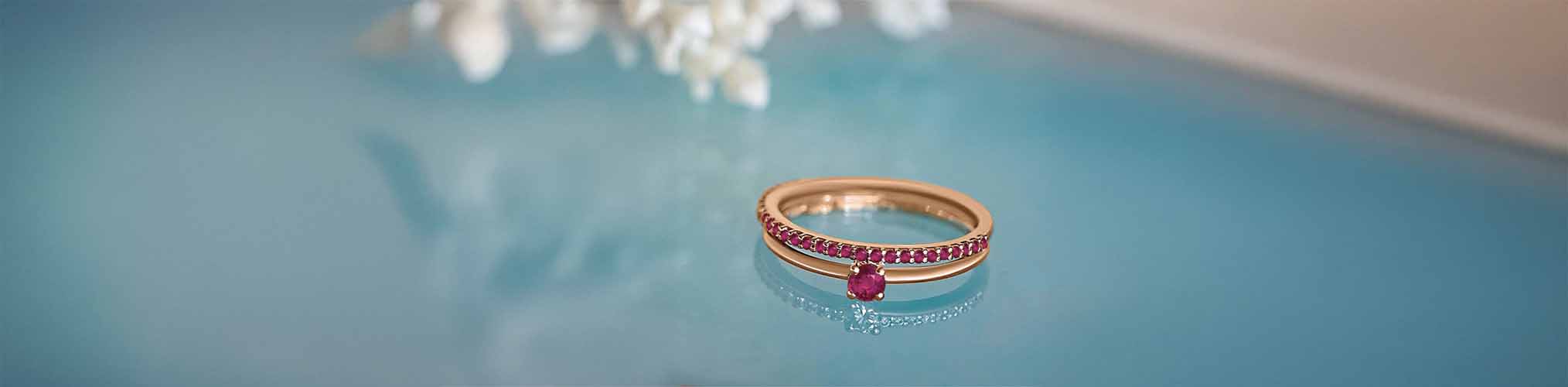 Rose gold engagement ring set with ruby and pavé of red gemstones on aquatic blue background