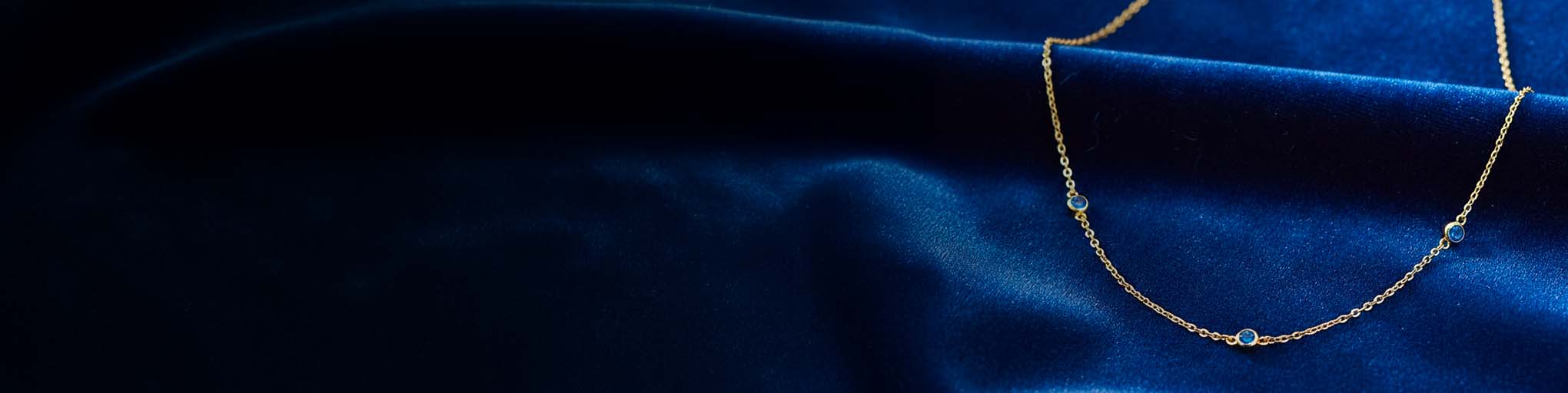 Vermeil blue sapphire necklace on fine golden chain positioned on luxurious navy blue silk French jewellery