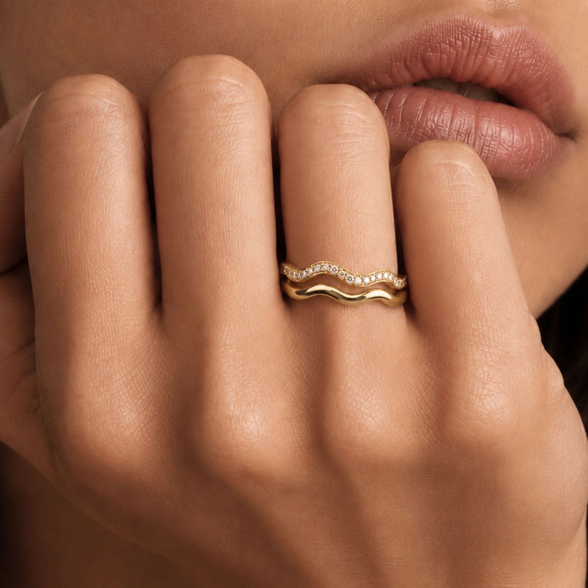 Thalassa wave wedding rings worn, hand near face, 18K yellow gold