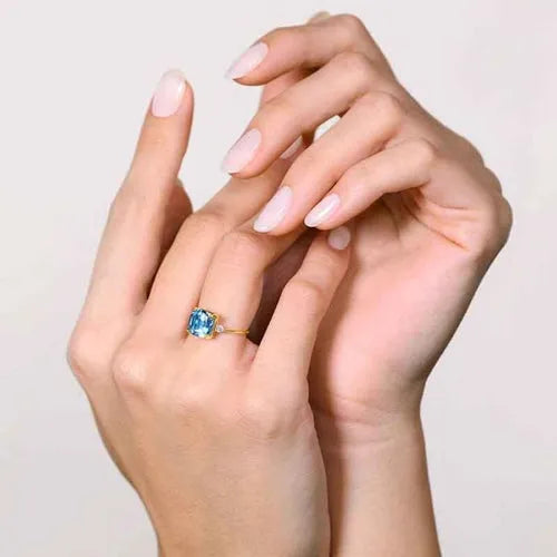 A cushion-cut blue topaz ring in yellow gold, worn on the hands