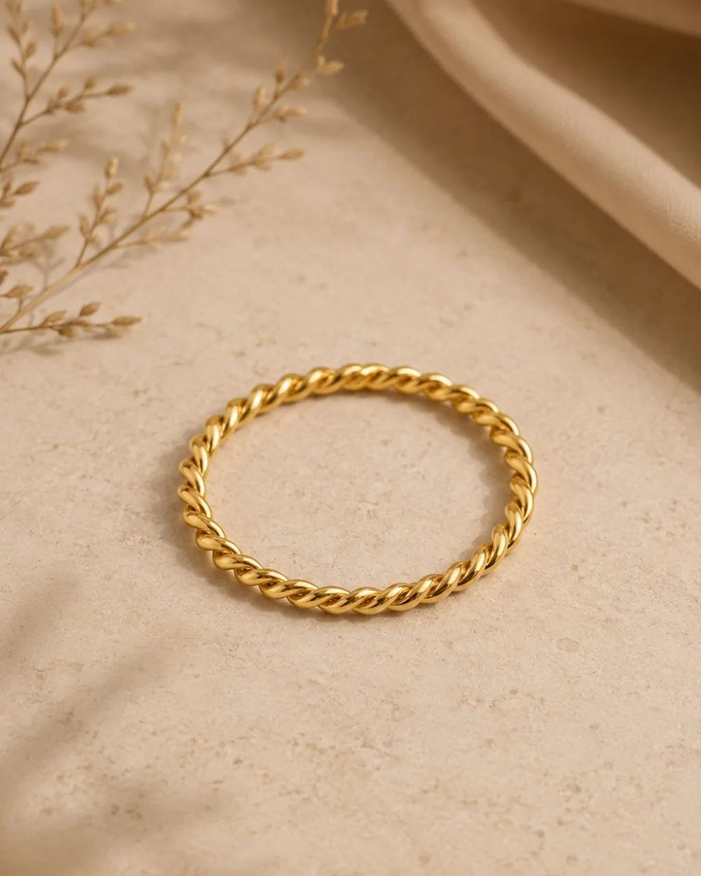 Alliance torsadée Musubi en or jaune 18 carats posée sur fond beige naturel par Mayuri