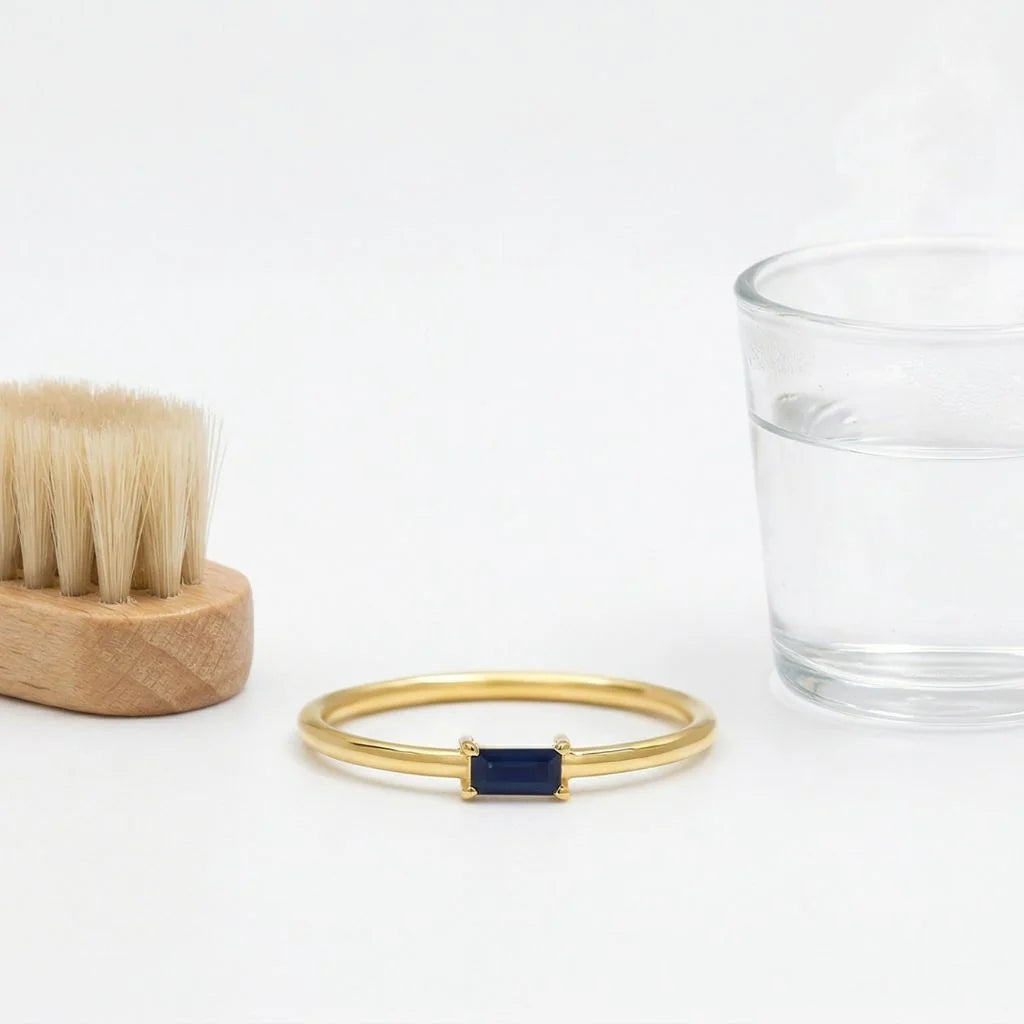 18K Yellow Gold ring set with a baguette Sapphire, with a soft brush and a glass of lukewarm water
