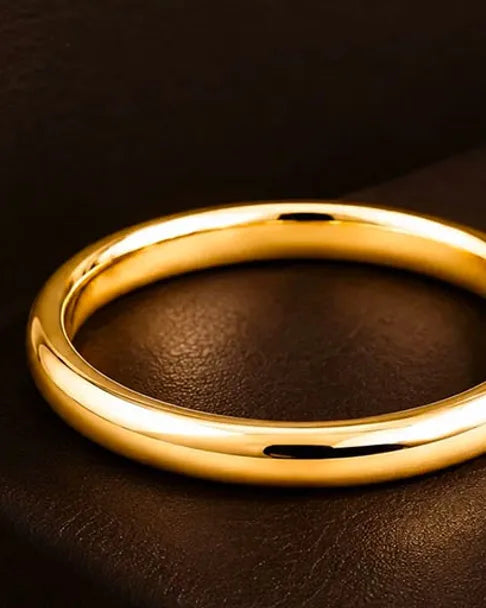 Solid 18K yellow gold wedding ring on dark brown leather, warm light highlighting the gold's brilliance