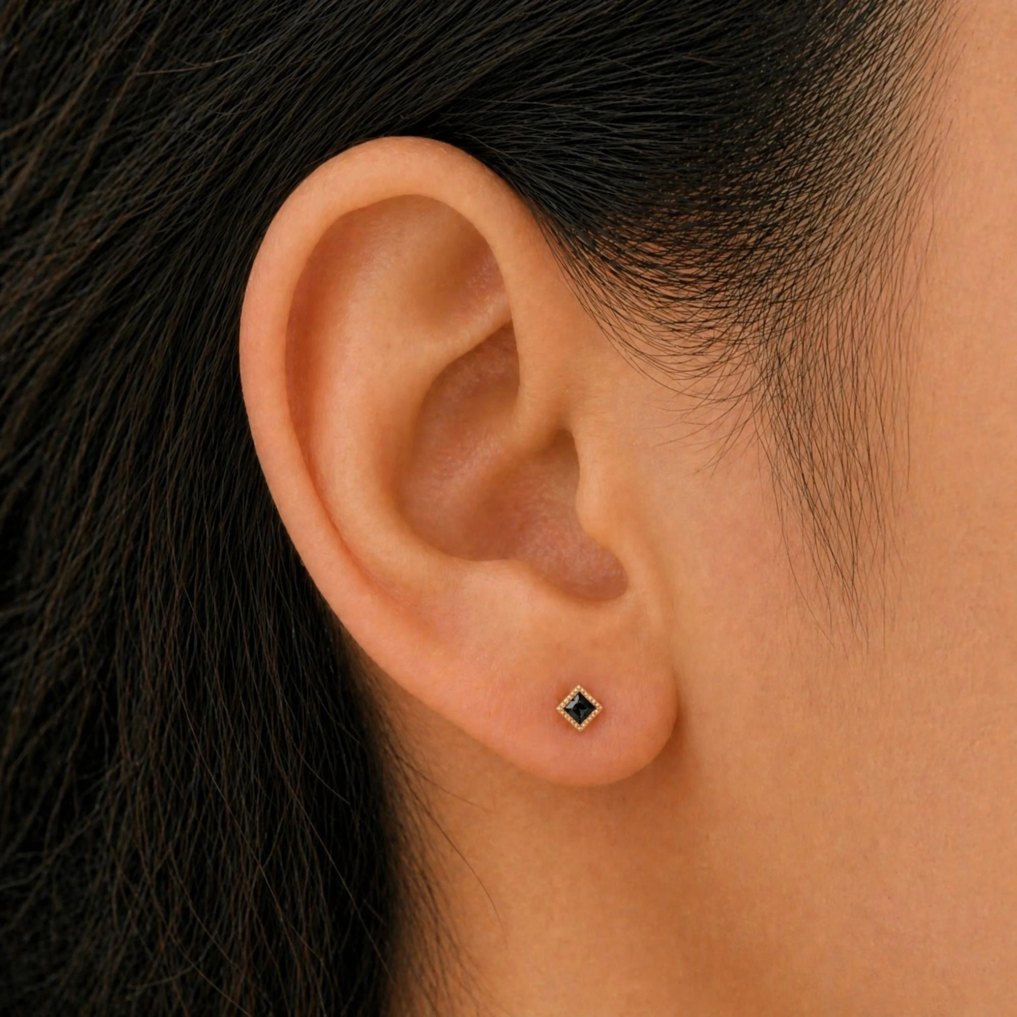 Indrani black diamond earrings worn on the ear, princess-cut stud in twisted rope setting, yellow gold