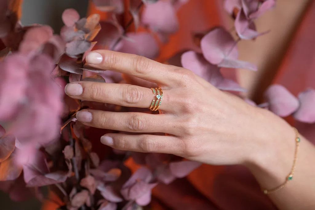 A collection of Emerald and Diamond rings set in 18K yellow gold by Mayuri, worn on the finger