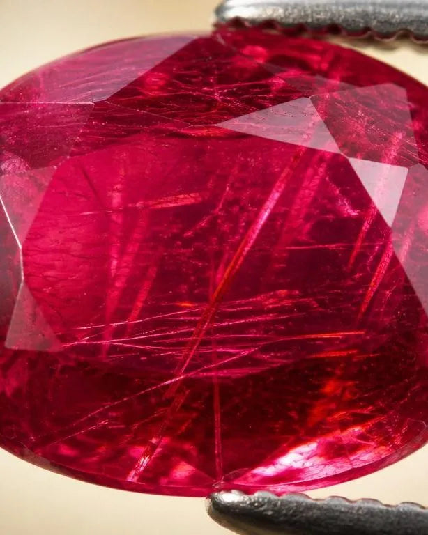 Rubis naturel tenu par pince gemmologique montrant des inclusions rutile visibles à l'intérieur